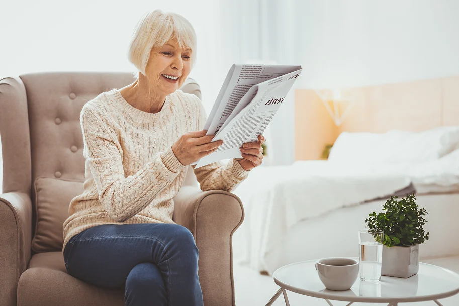 Vitale Seniorin liest entspannt in einem hellen, modernen Wohnzimmer eine Zeitung
